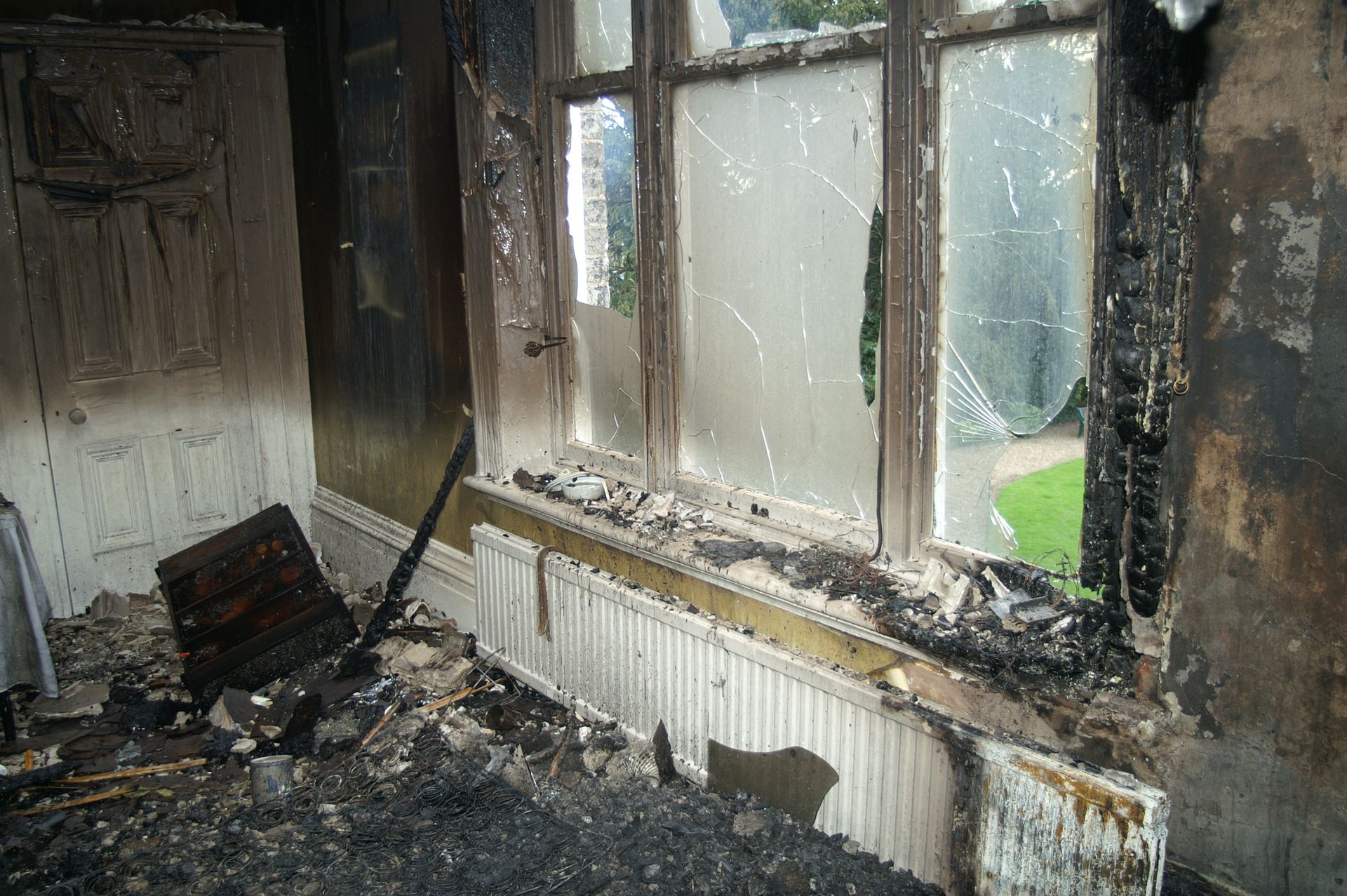 Burned, smoke-damaged room with charred walls, broken window, and debris on the floor