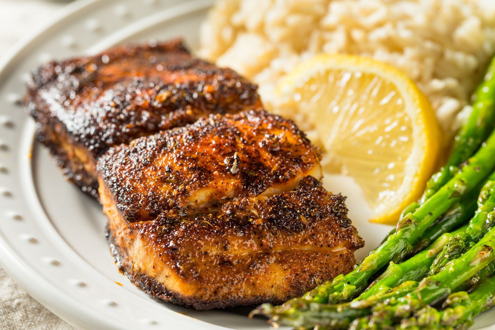 Grilled salmon with lemon, rice, and asparagus on a white plate