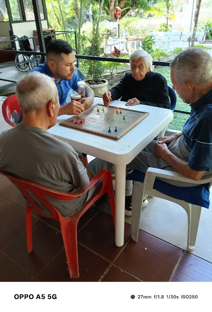 Cuatro personas juegan a un juego de mesa alrededor de una mesa blanca en un patio cubierto.