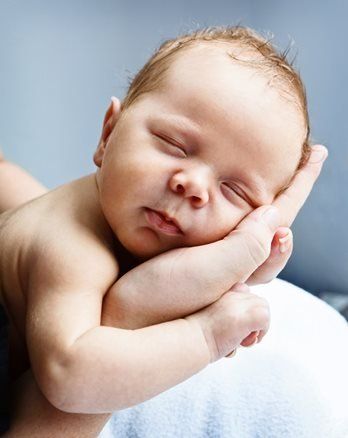 Adult kissing baby’s forehead while holding them close outdoors