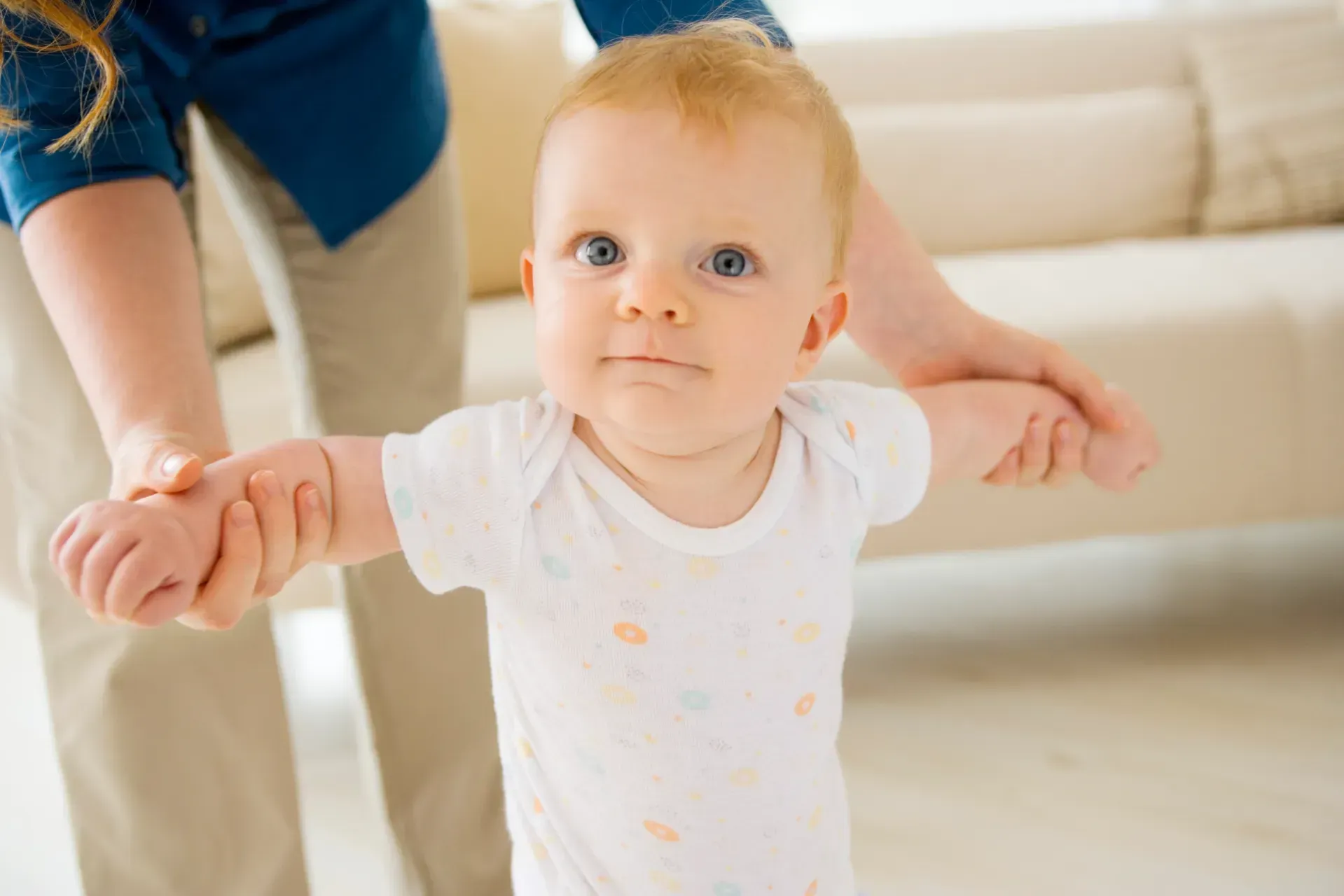 A baby is holding a woman 's hand while trying to walk.
