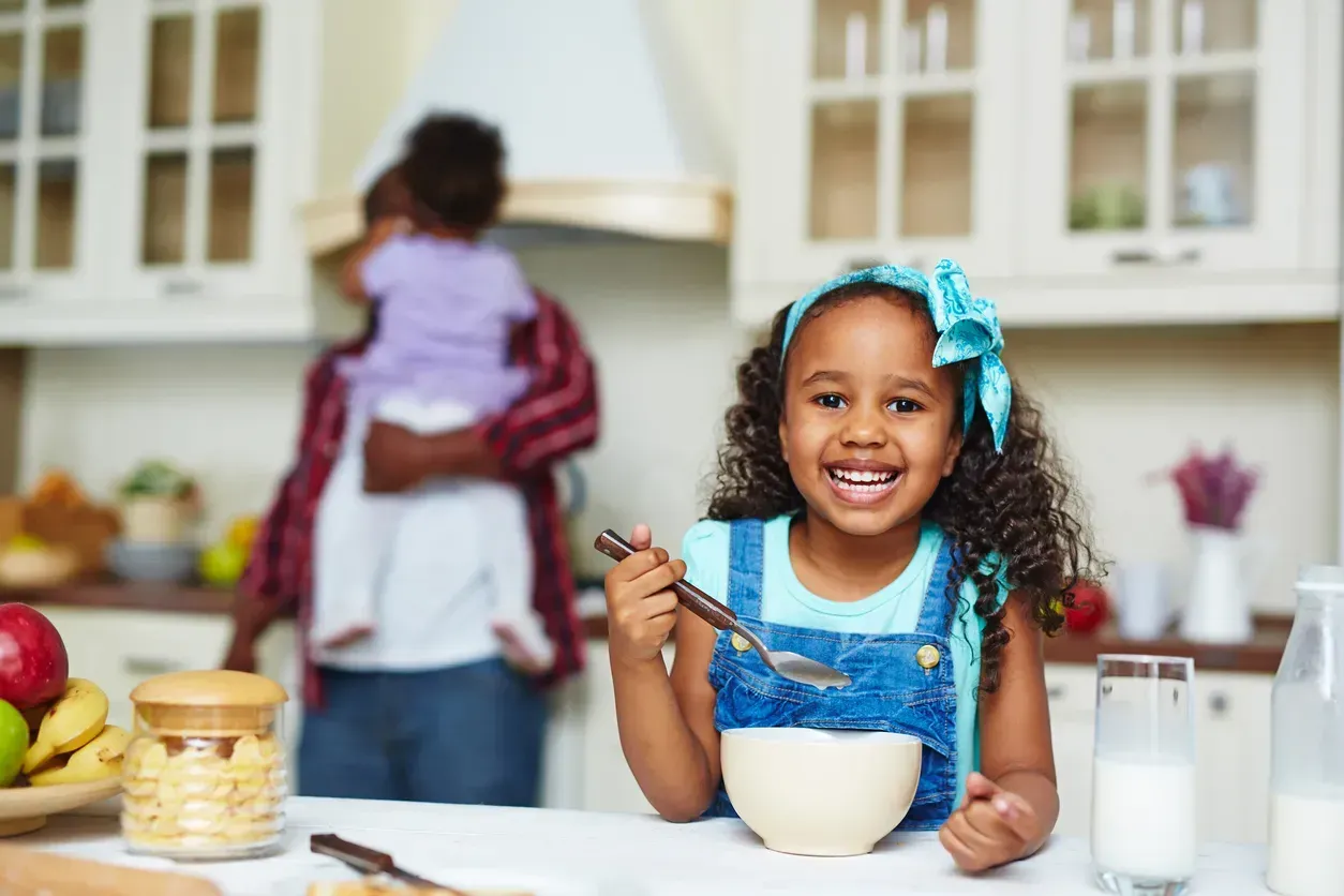 A little girl is sitting at a table eating cereal with a spoon.