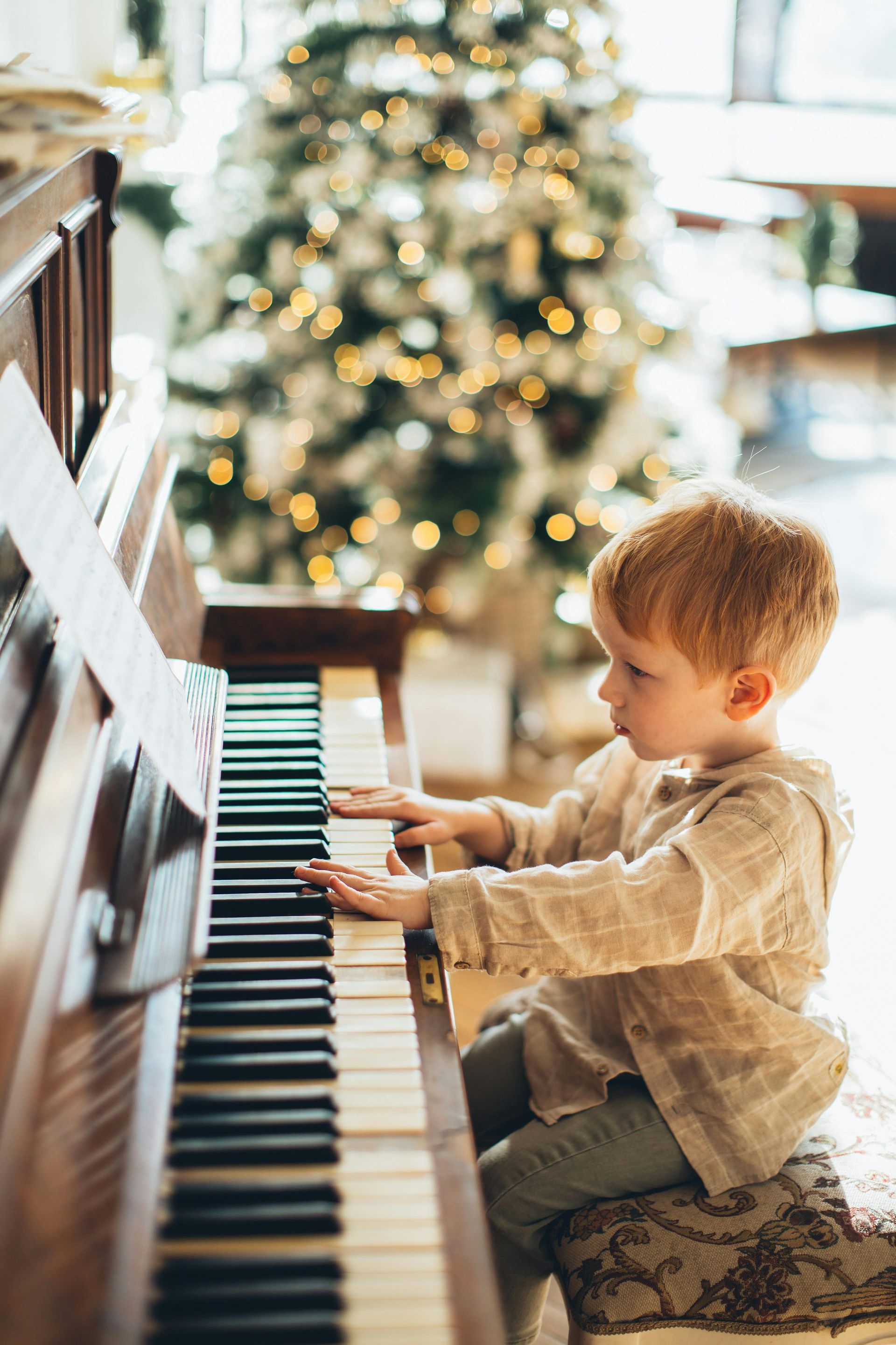 Young child with red hair playing piano, Christmas tree in the background.