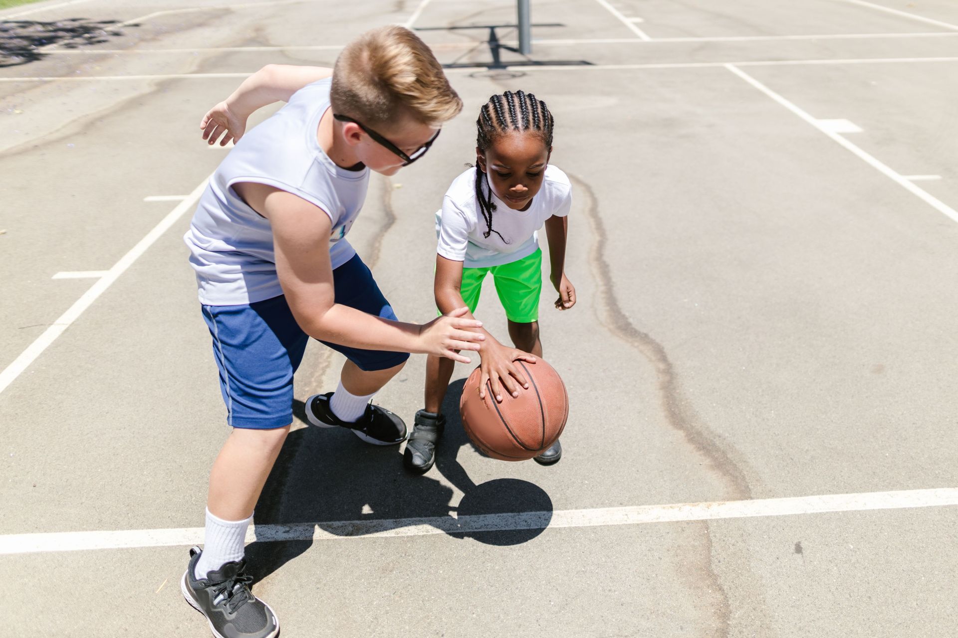 Two children dribbling a basketball on an outdoor court