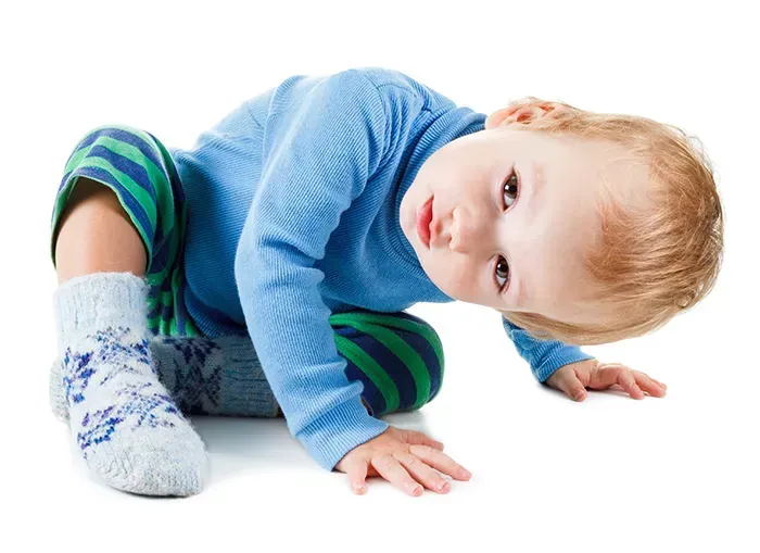 A baby in a blue shirt and green striped pants is crawling on the floor.