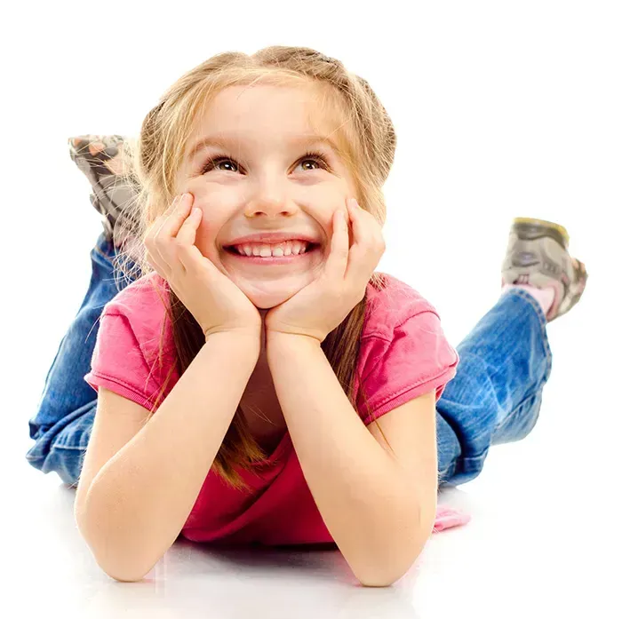Girl in pink shirt and jeans smiling, looking up, resting head on hands.
