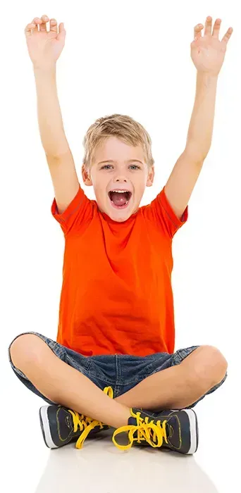 A smiling boy is raising his arms in the air