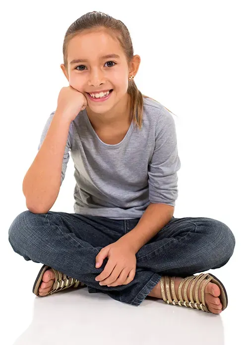 A boy is sitting cross legged on the ground with a fist under his chin