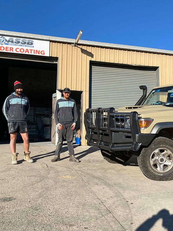 Two Men Are Standing Next to A Truck in Front of A Building — ASSB Armidale Sand And Soda Blasting In Armidale, NSW