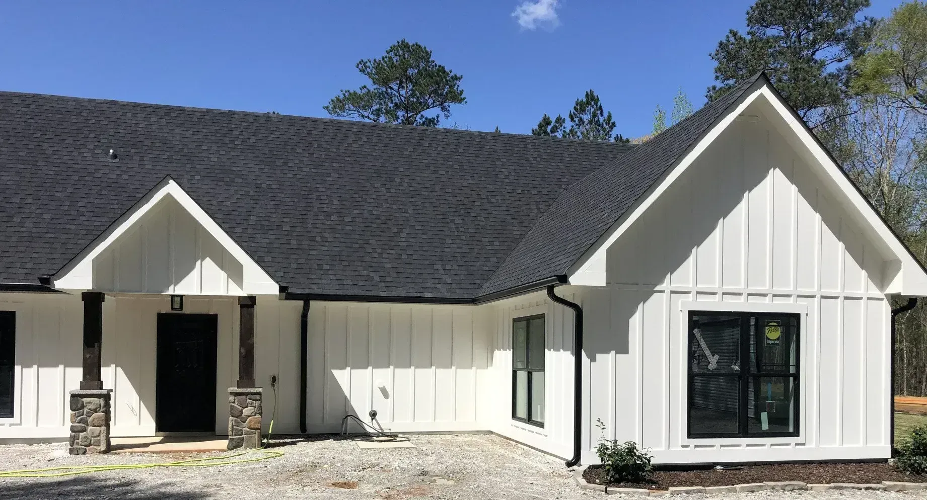 White single-story house with dark roof, front porch, and black-framed windows under a blue sky