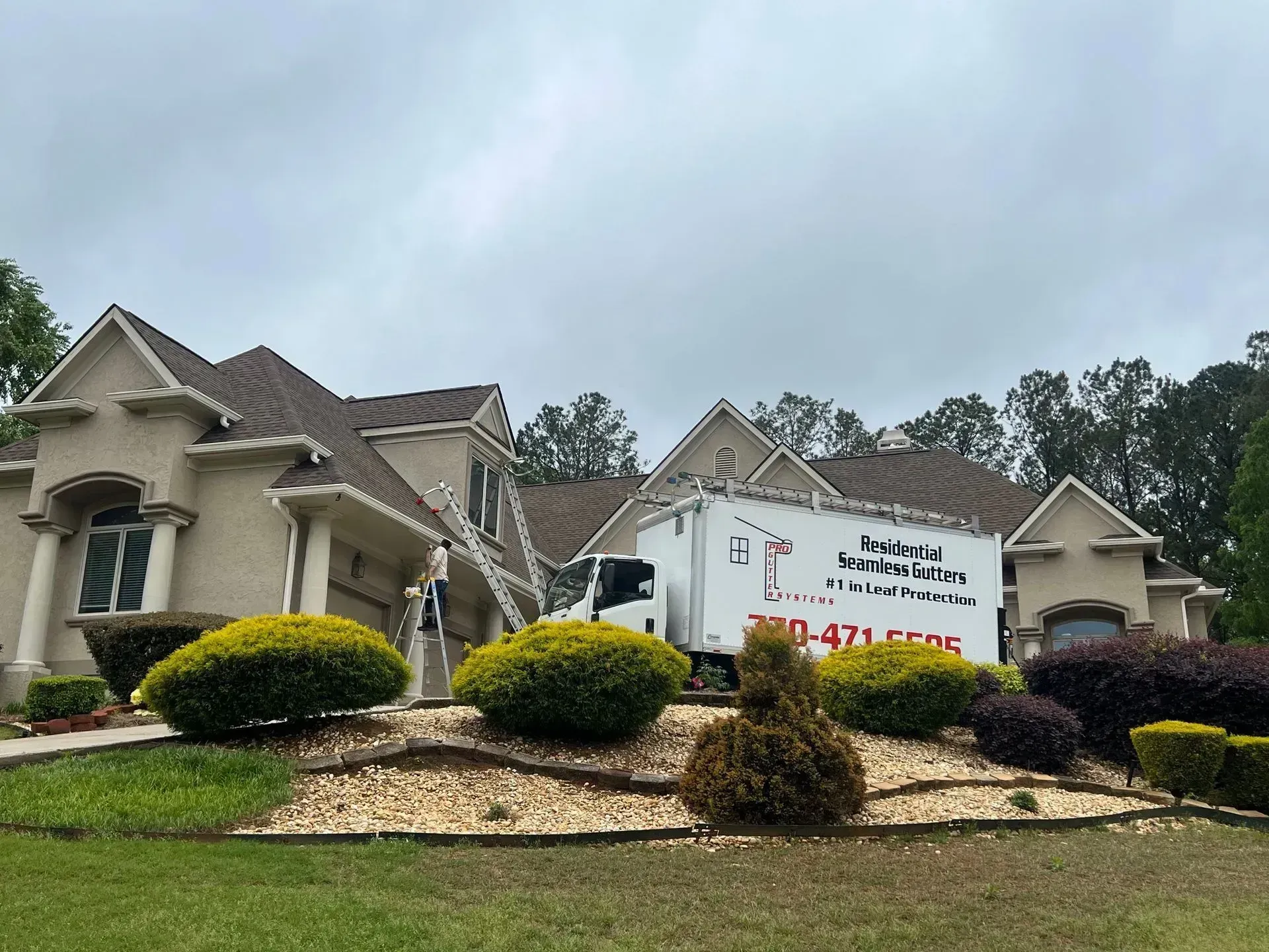 Stately house with a large real estate sign and landscaped front yard under cloudy sky