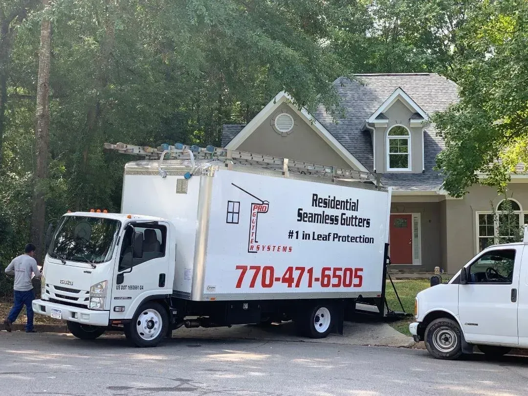 White moving truck with company logo and phone number parked by a house, with workers nearby