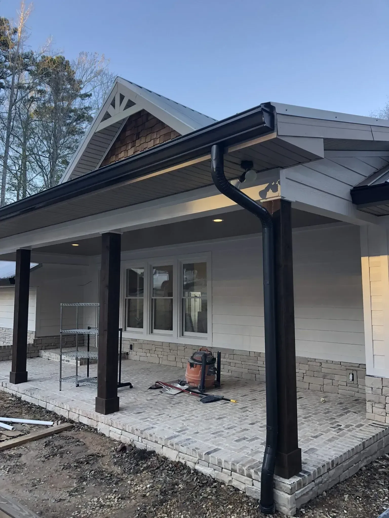 Covered porch on a stone house under construction, with black columns and gutters.