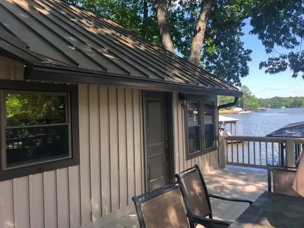 Lakefront cabin deck with chairs, brown siding, and a metal roof overlooking the water