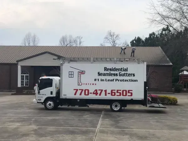 White box truck with “Residential Seamless Gutters” parked outside a building with a ladder on top.