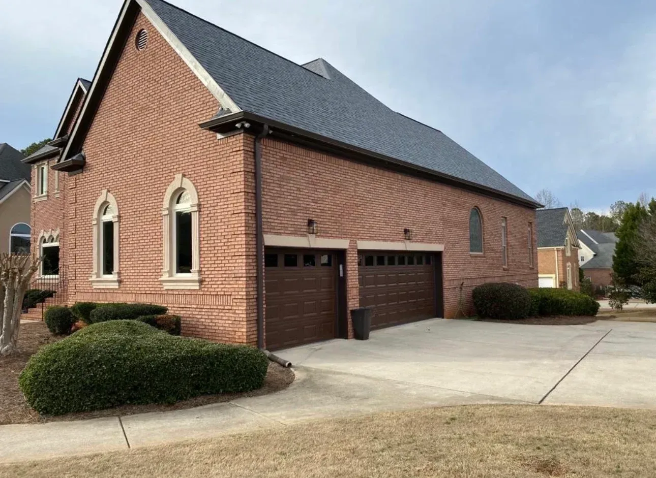 Brick house with dark roof, arched windows, and double garage on a concrete driveway.