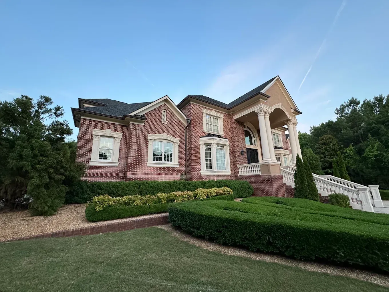 Brick house with white trim, front porch, and manicured lawn on a landscaped hillside
