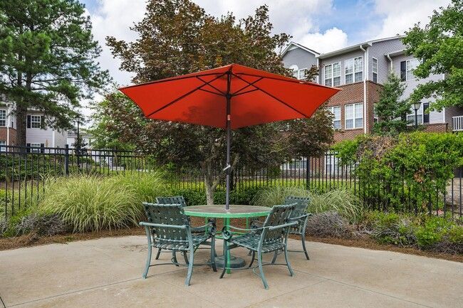 An outdoor patio with an orange umbrella, table, and chairs. Buildings and foliage in the background.
