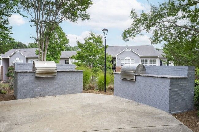 Two outdoor grills set in gray brick structures, with buildings and trees in the background.