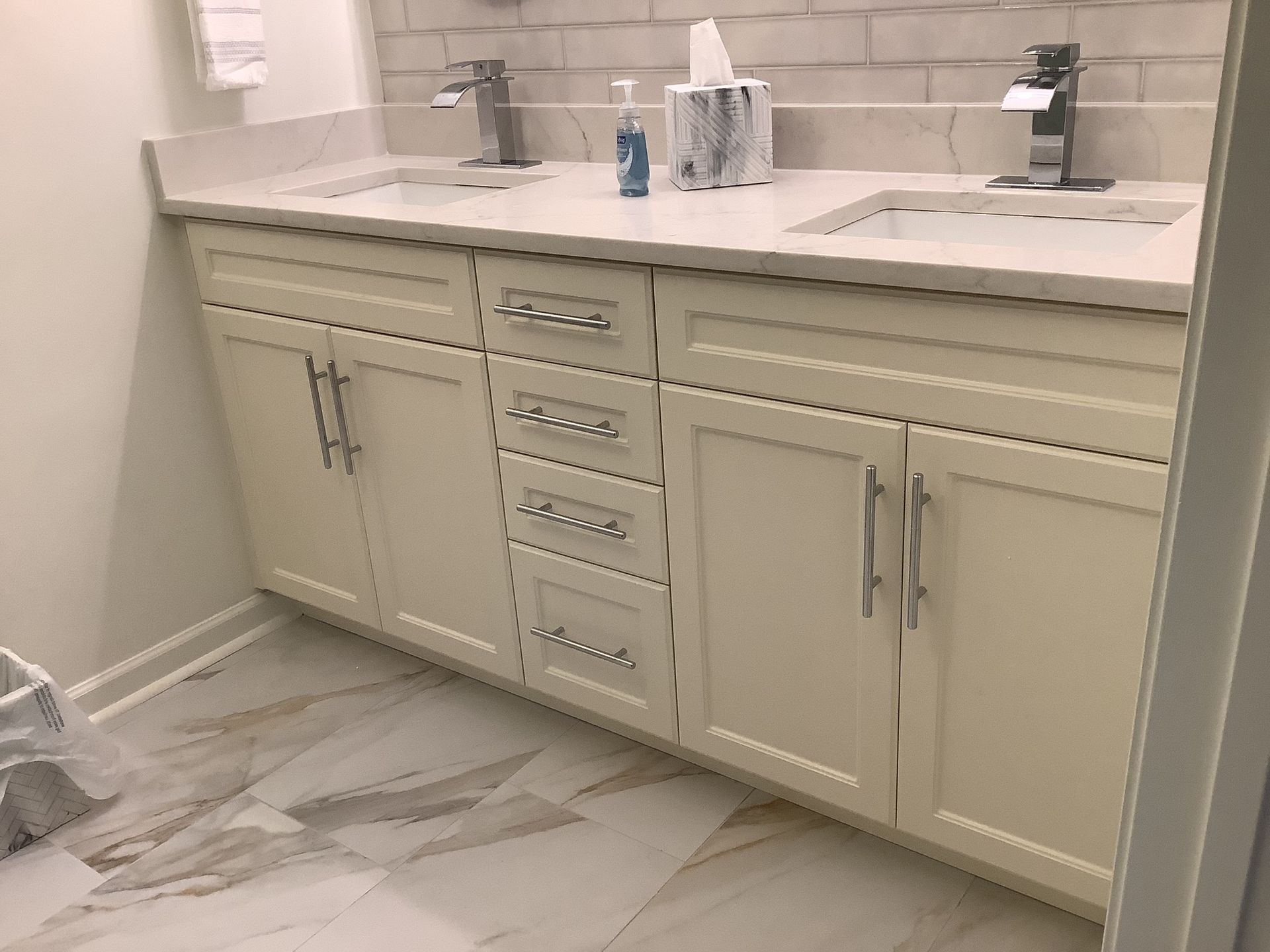 Cream bathroom vanity with double sinks, white countertop, and marble floor tiles.
