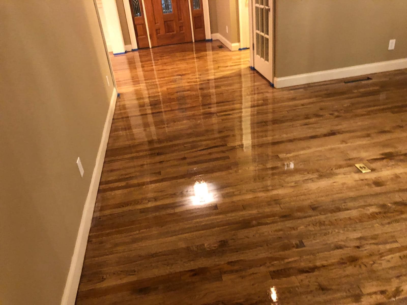 Shiny hardwood hallway leading to a doorway, with beige walls and a reflective floor.