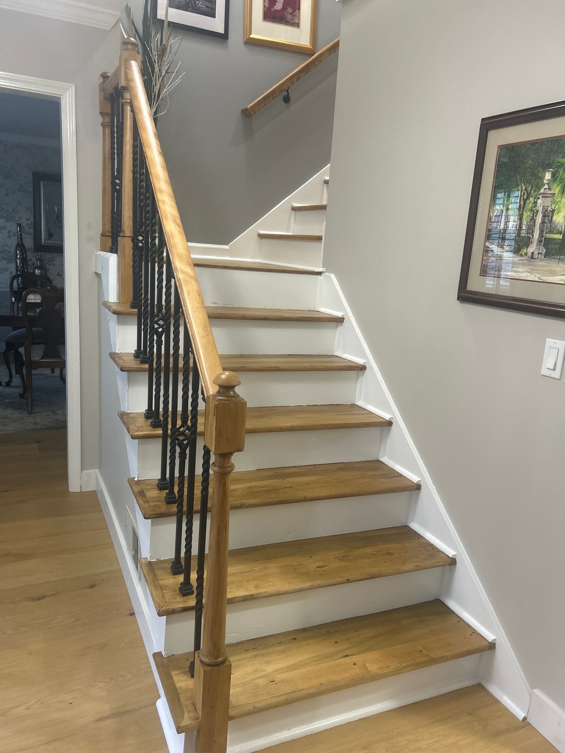 Indoor staircase with white risers, wood steps, and black handrails in a home hallway