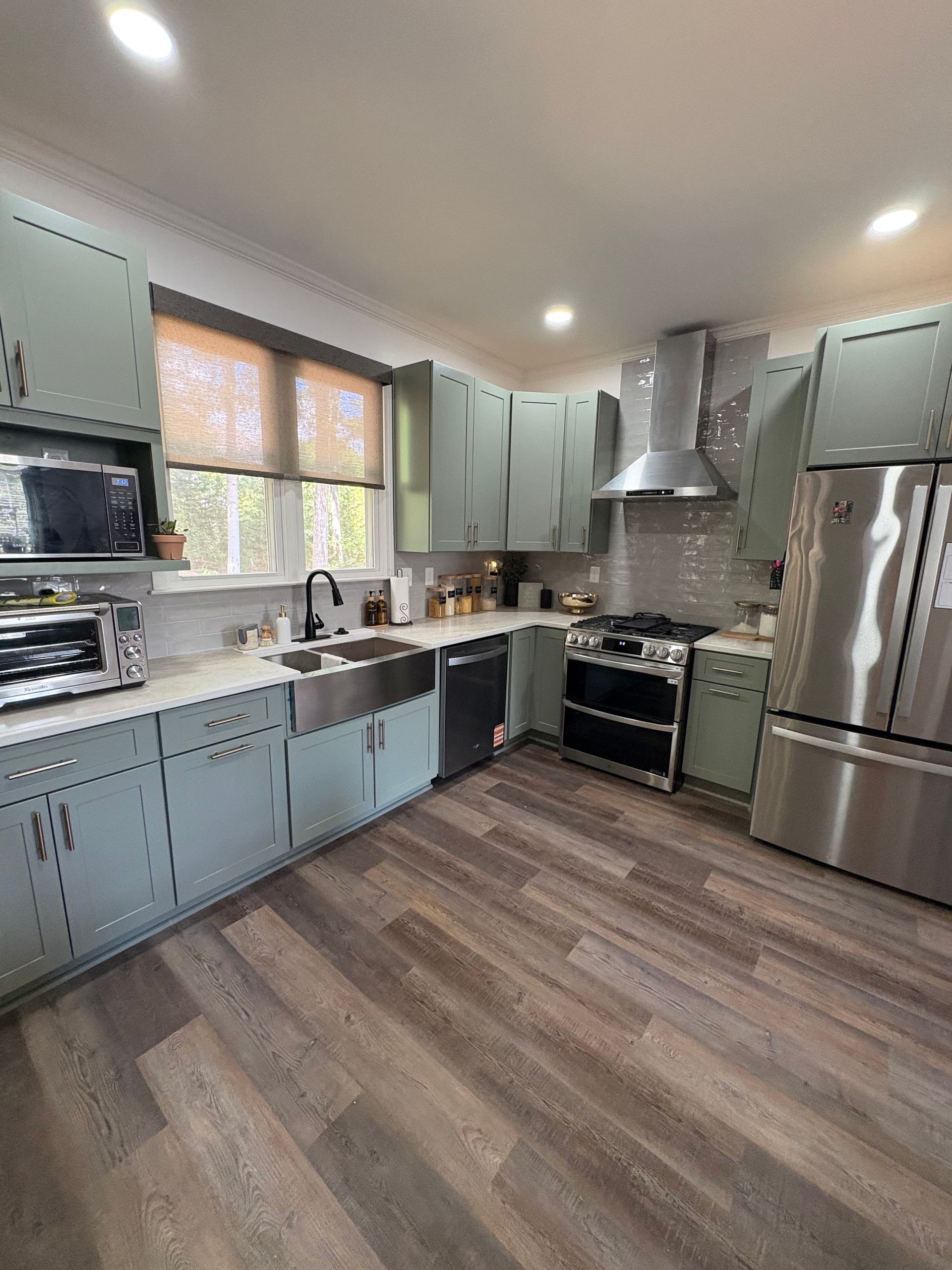 Modern kitchen with mint cabinets, stainless steel appliances, and wood-look flooring