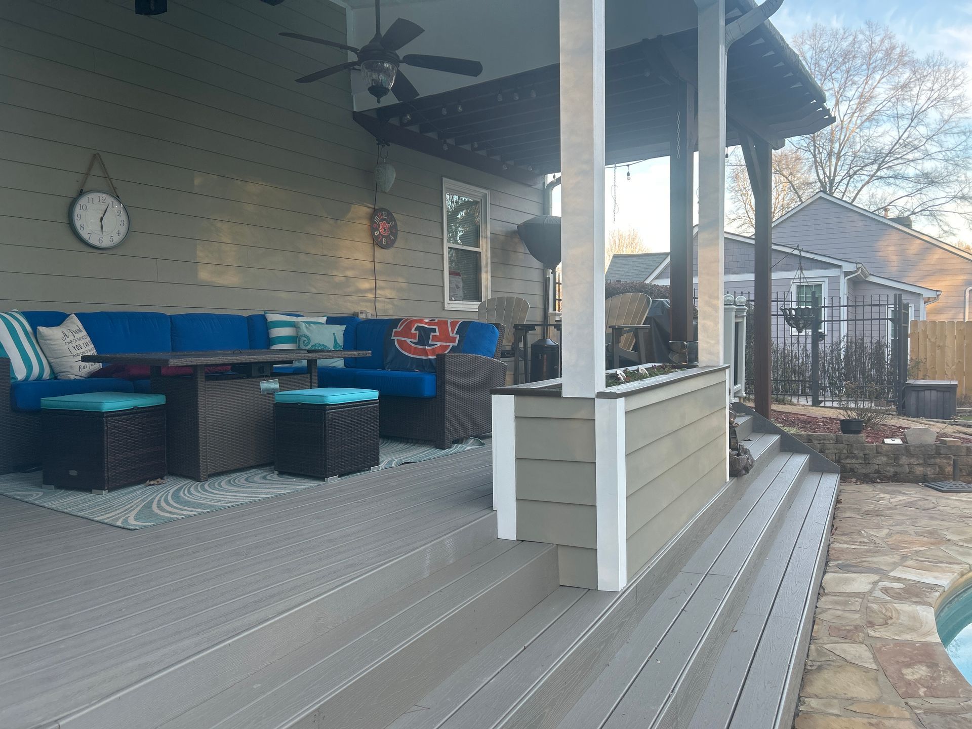 Covered backyard patio with blue-and-black outdoor seating, gray deck flooring, and a small side table.