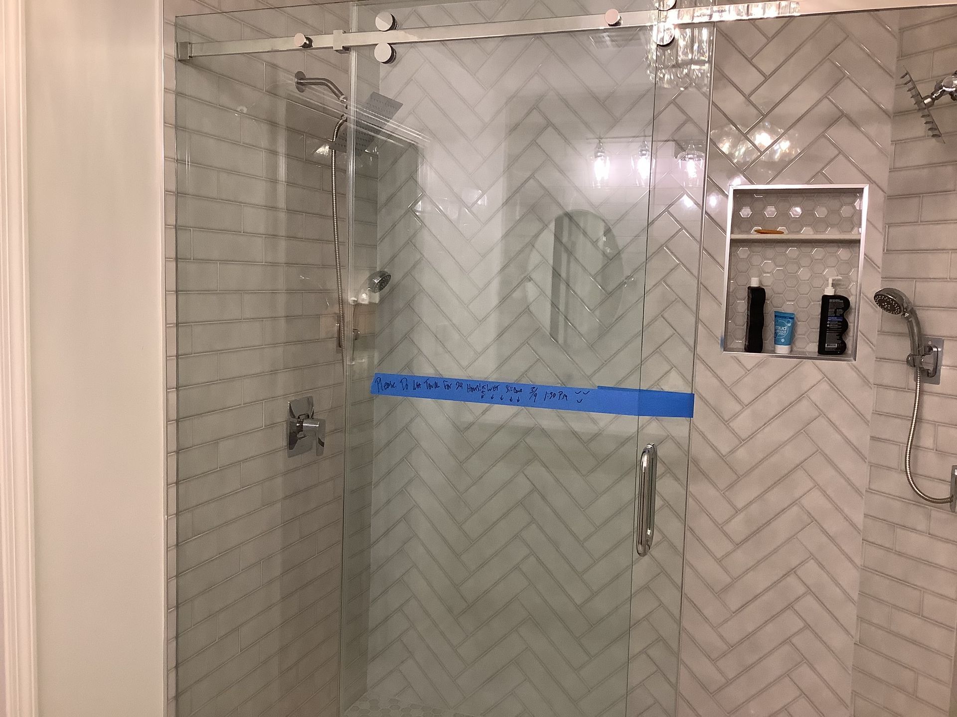 Glass shower enclosure with tiled walls, chrome fixtures, and a blue tape line across the door