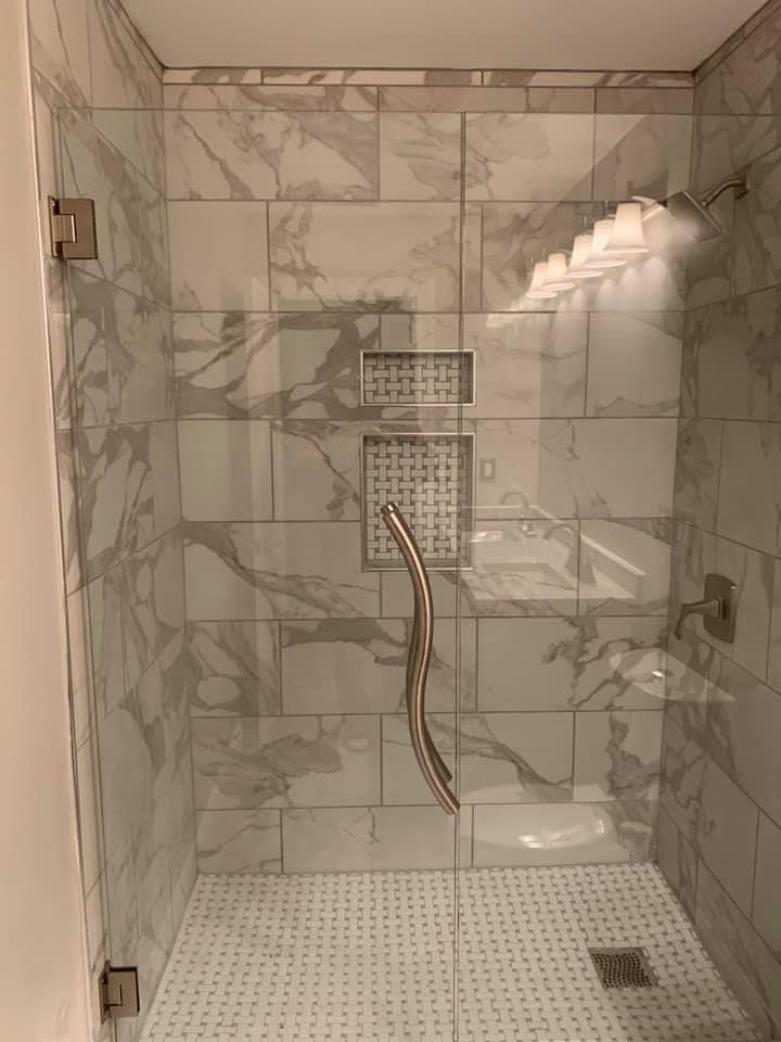 Empty marble-tiled shower with grab bars, bench, handheld showerhead, and pebble floor.