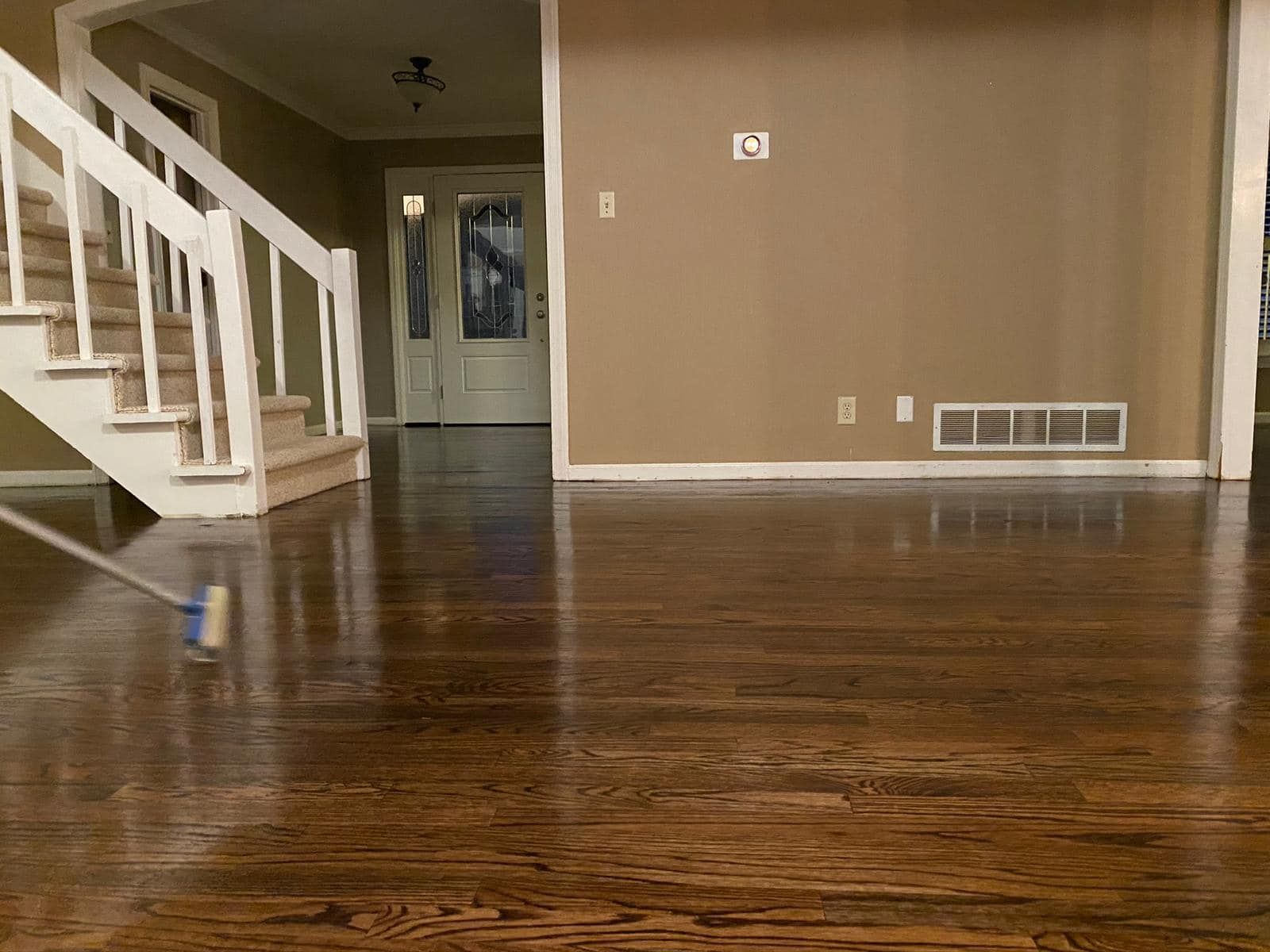 Empty living room with dark hardwood floors, beige walls, white staircase, and a doorway in the back.