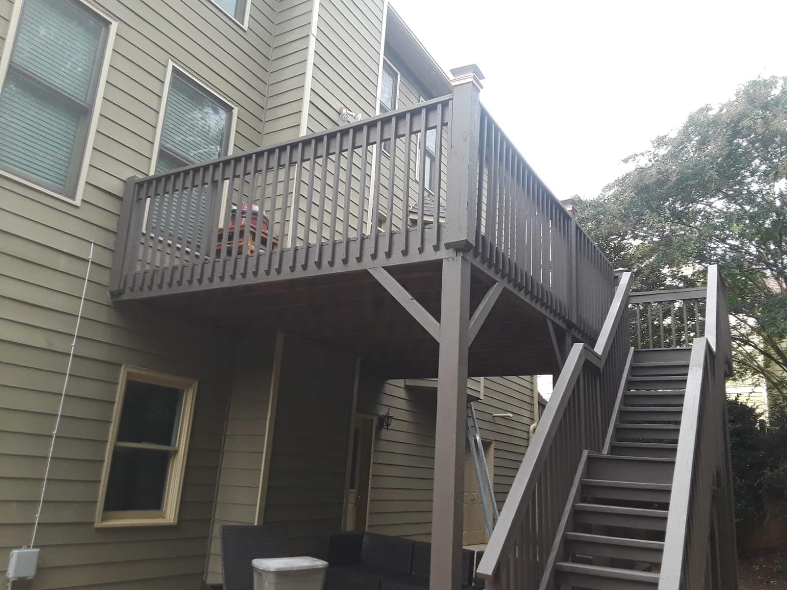 Outdoor apartment stairway and elevated wooden deck with railing beside a beige house.