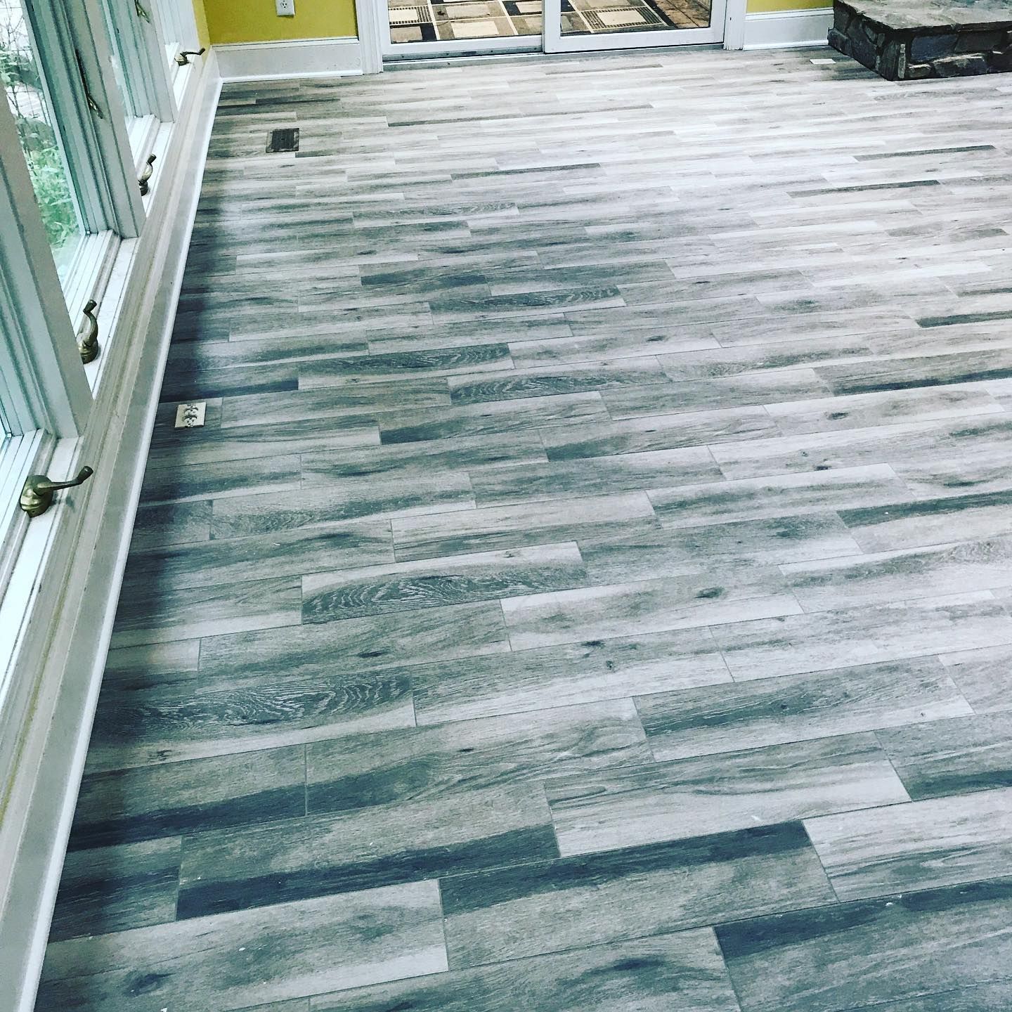 Light gray wood-look flooring in a bright room with large windows along the left wall.