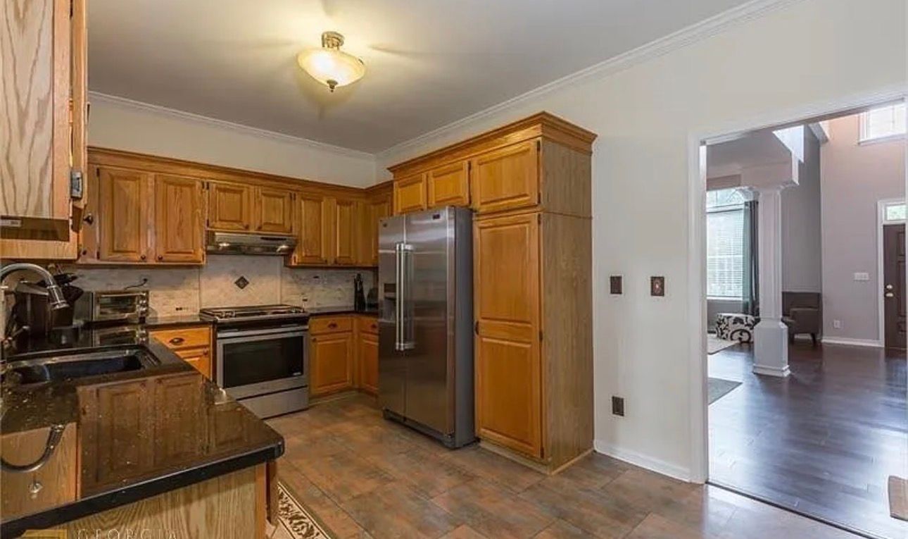 Spacious kitchen with wood cabinets, stainless steel fridge, and view into a bright adjoining room