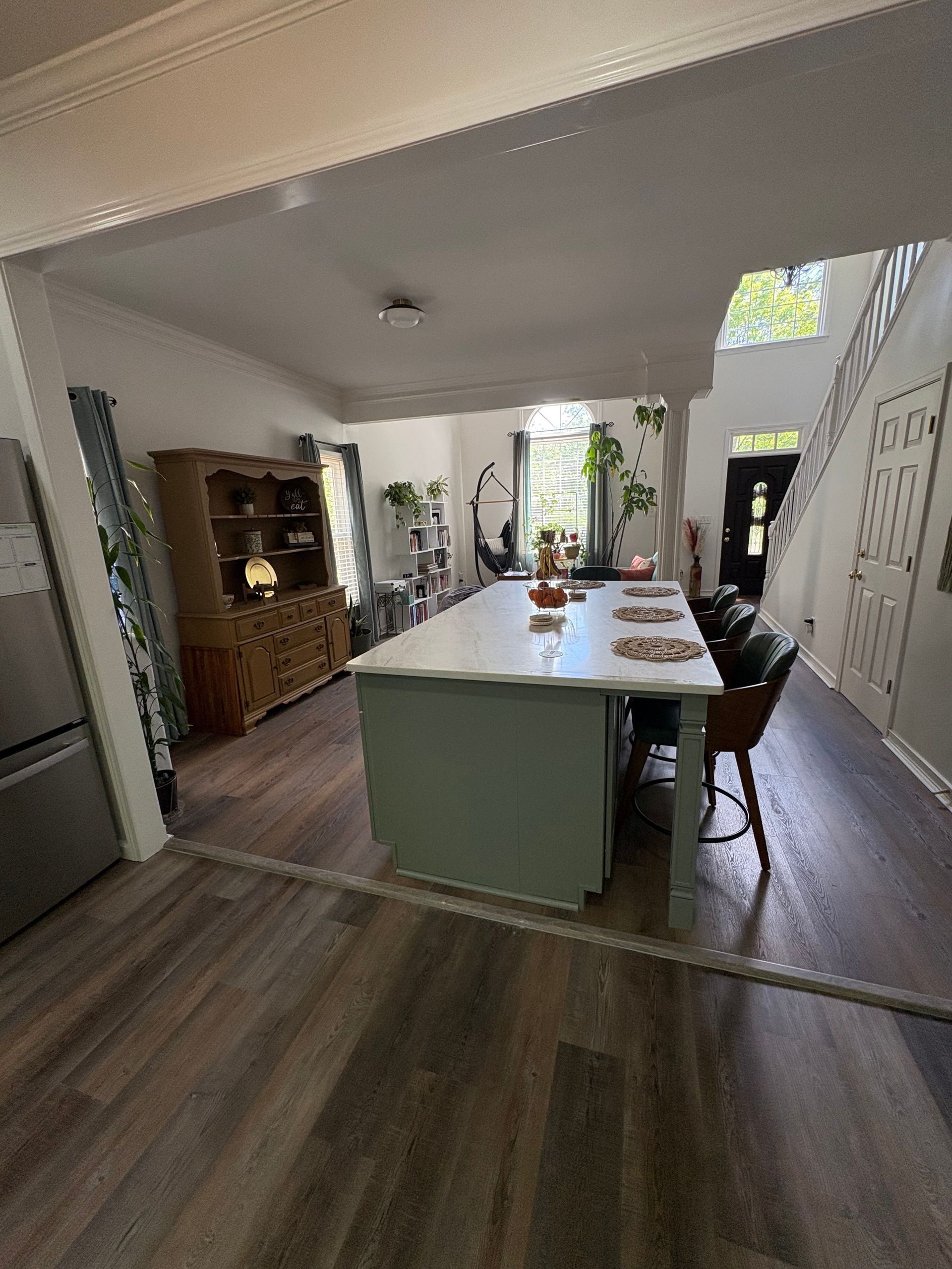 Bright kitchen with a large island, wood flooring, white walls, and dining area in the background.
