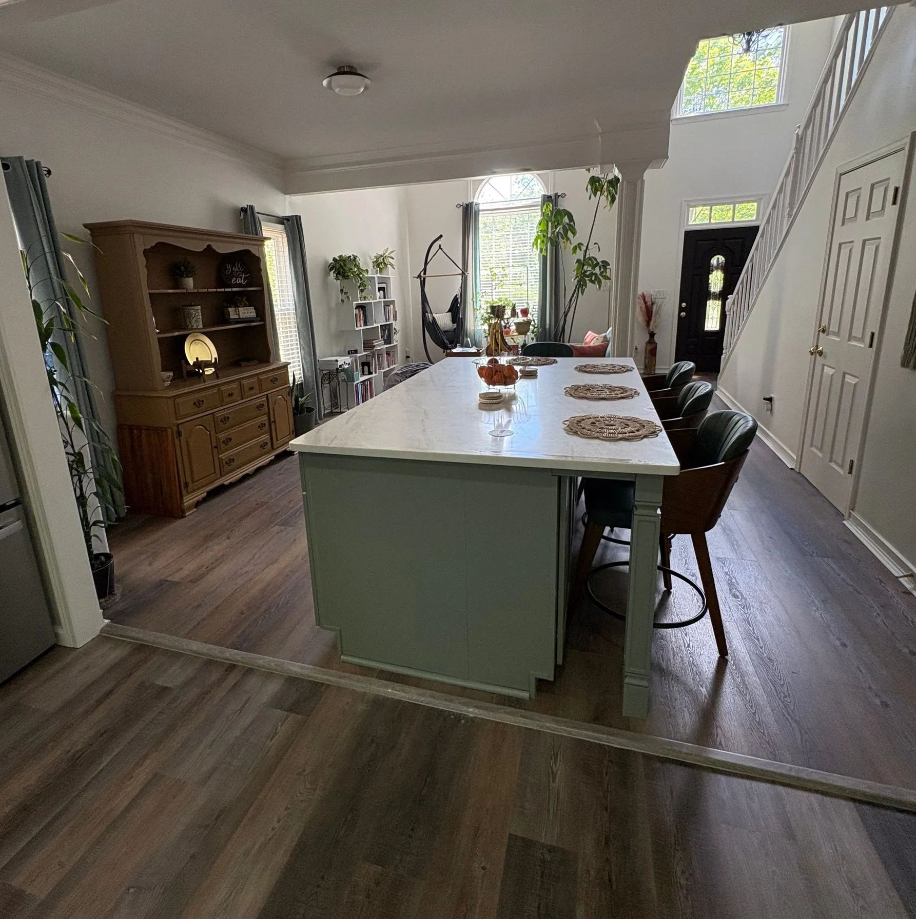 Open-plan dining room with a long white table, dark chairs, and wood flooring near a staircase