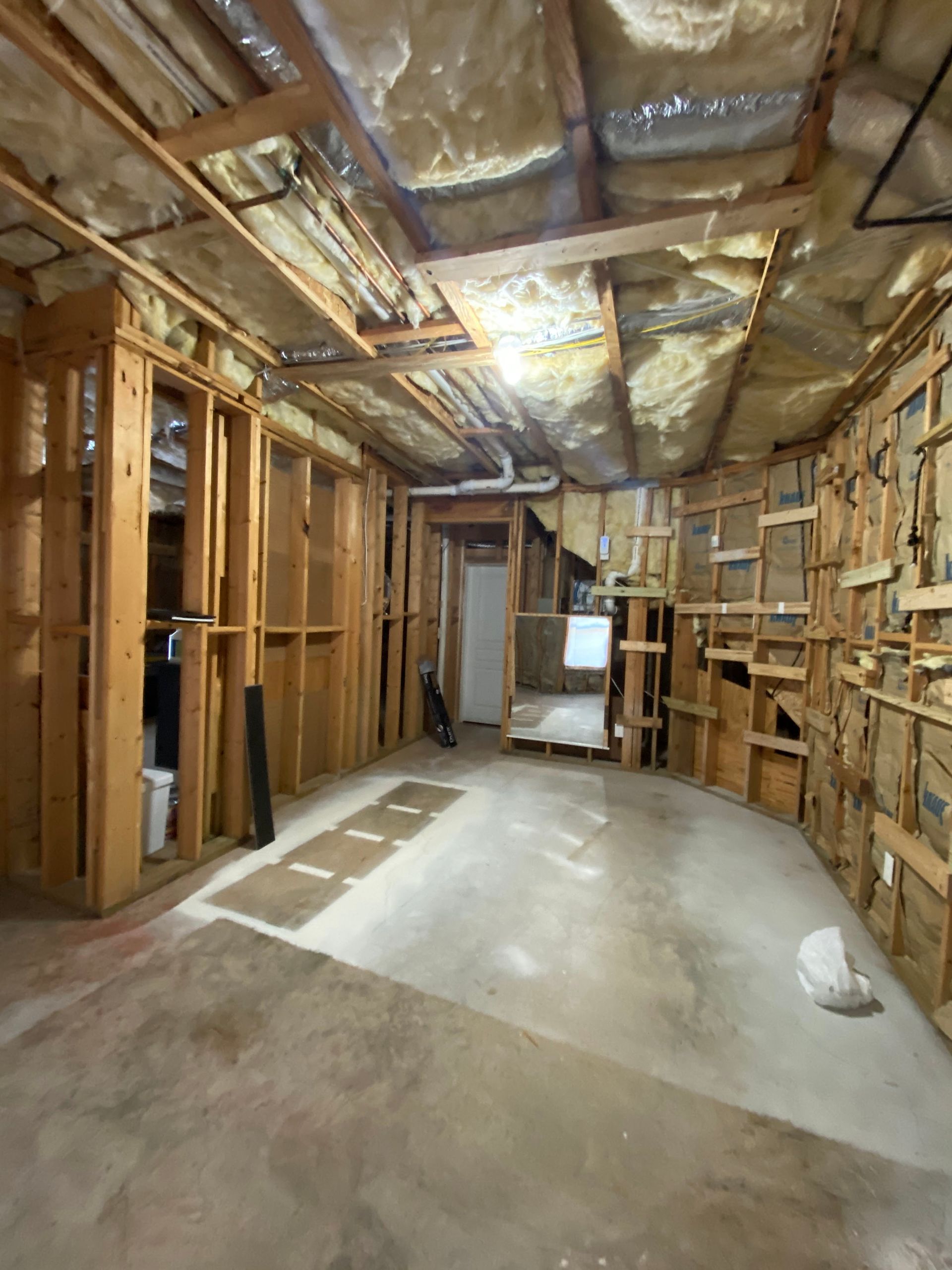 Unfinished basement with exposed studs, insulation, and concrete floor under renovation