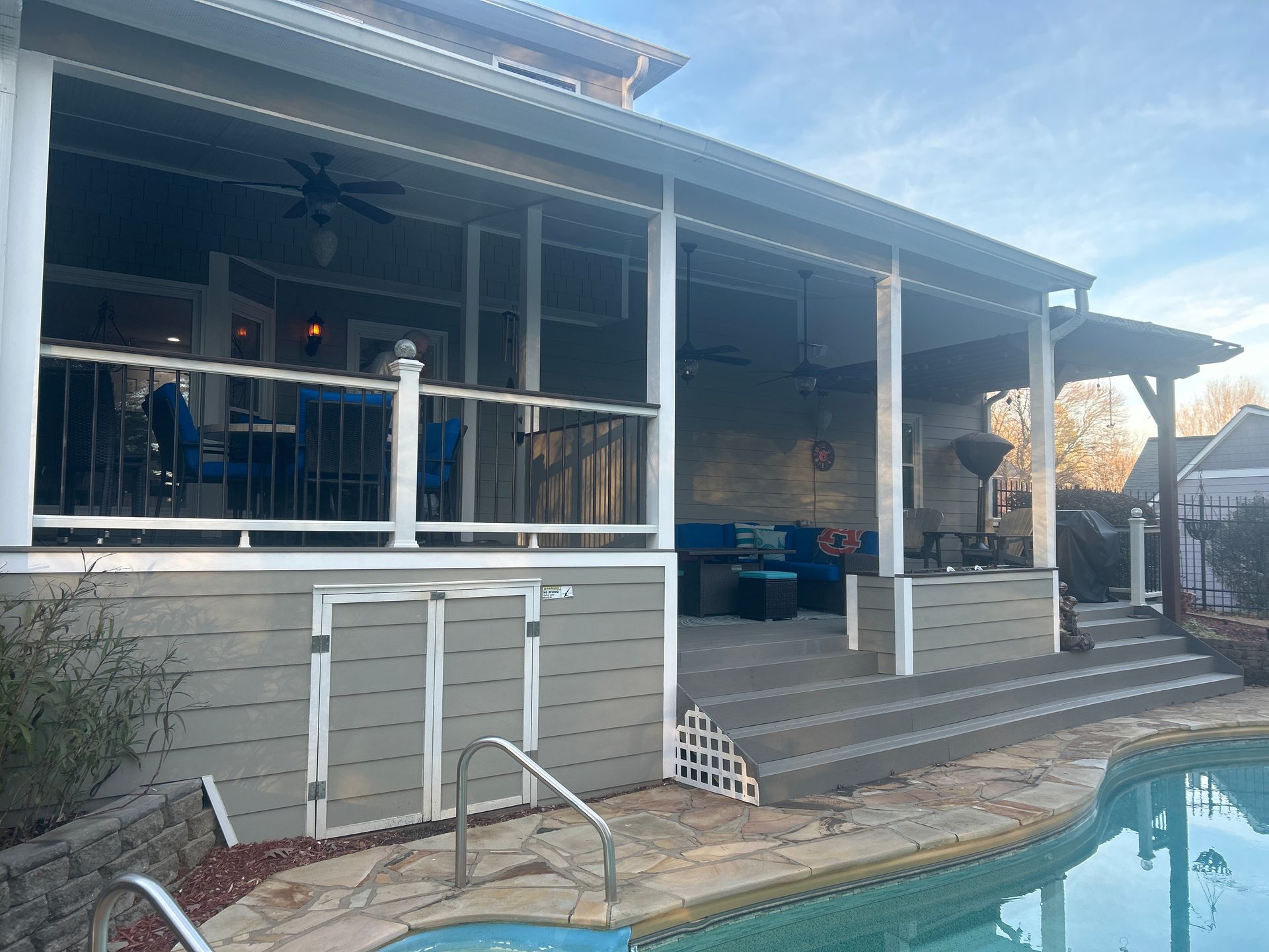 Back patio with covered deck, steps, and a pool beside a house at sunset