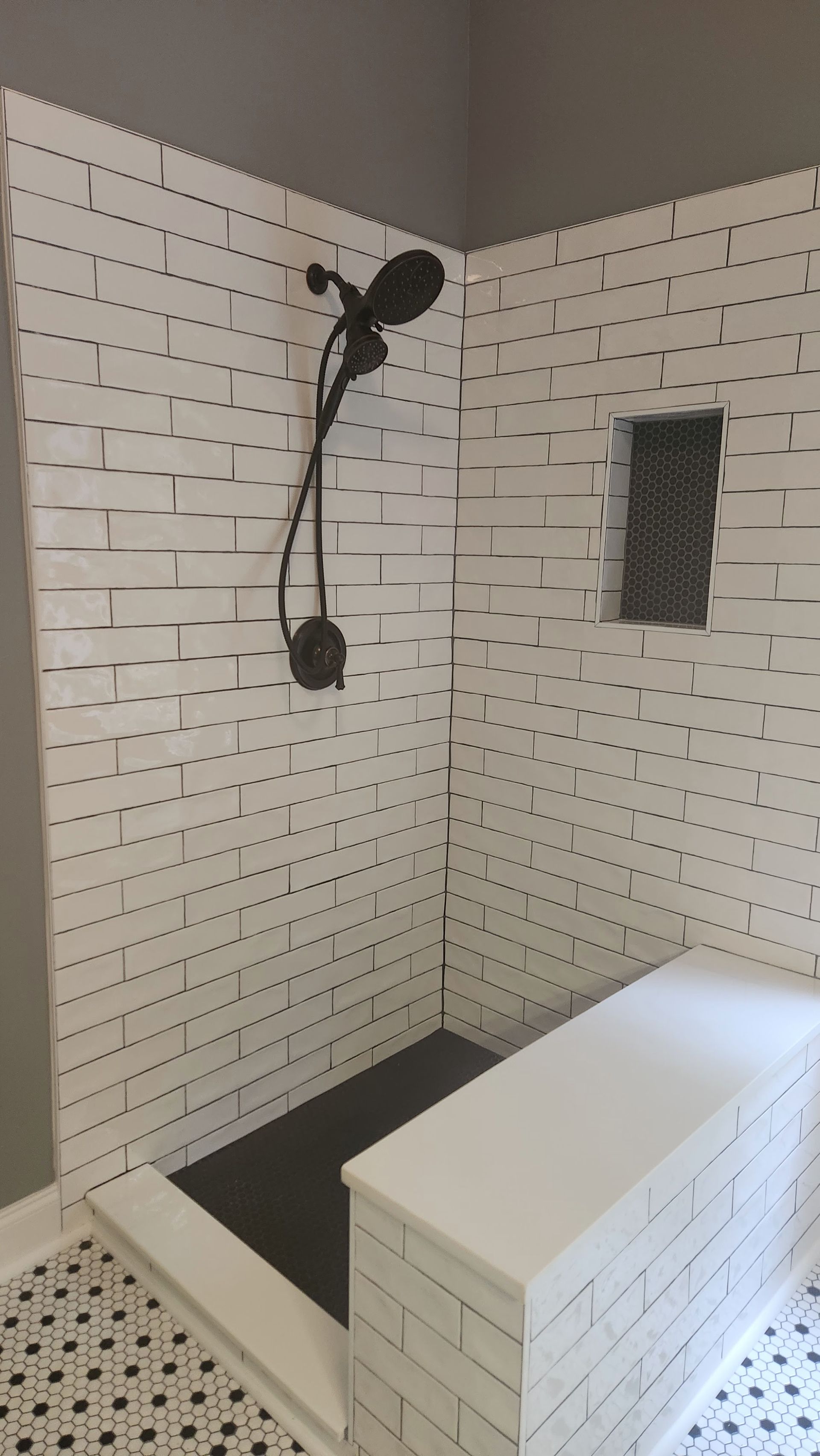 White tiled shower with black fixtures, built-in bench, and a small window on the right.