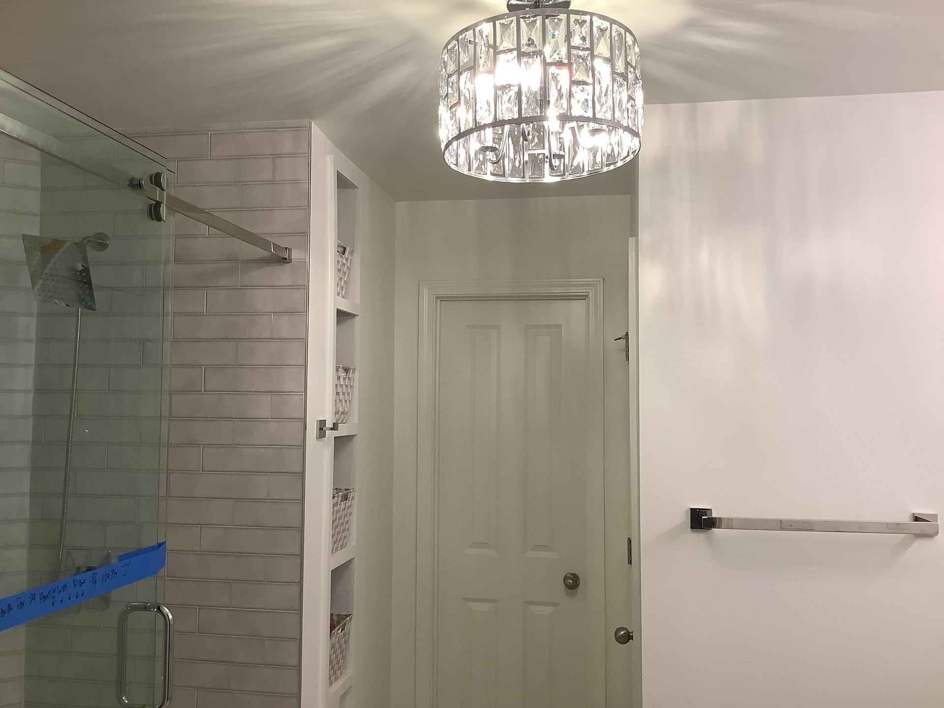 Bathroom with glass shower, white door, towel bar, and crystal ceiling light fixture