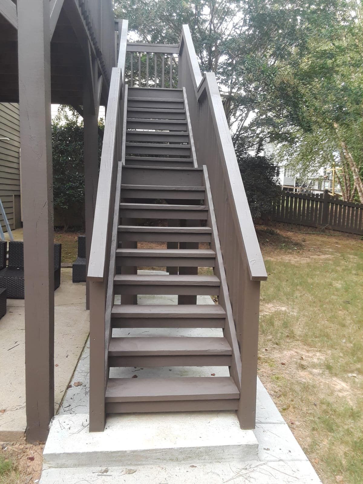 Outdoor wooden staircase with white railings leading to an elevated deck beside a house.