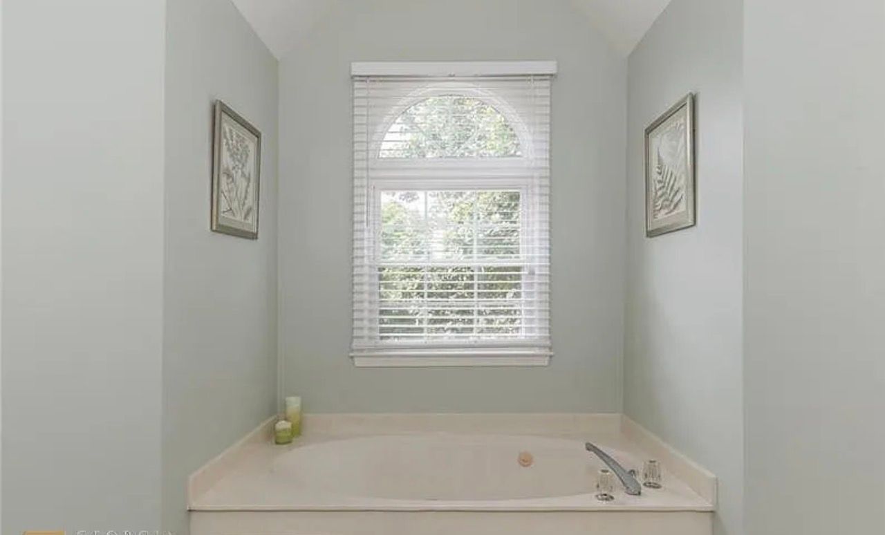 Bright bathroom with a soaking tub beneath a window and two framed wall pictures.