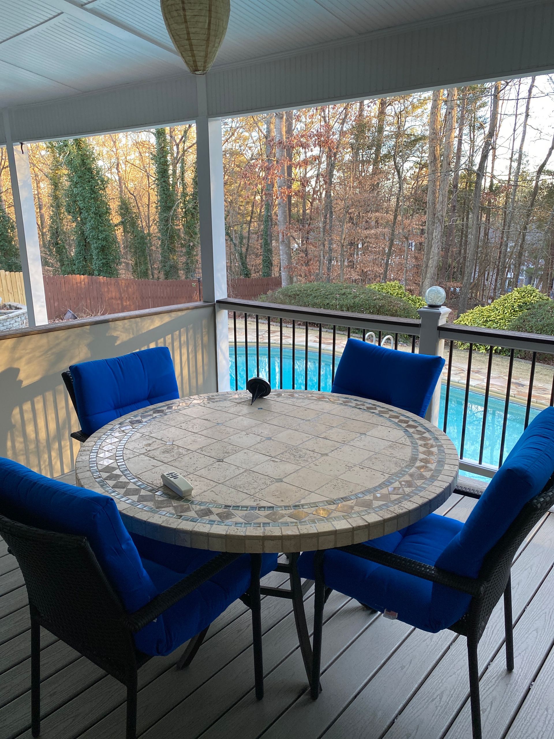 Patio table with four blue chairs overlooking a pool and autumn trees