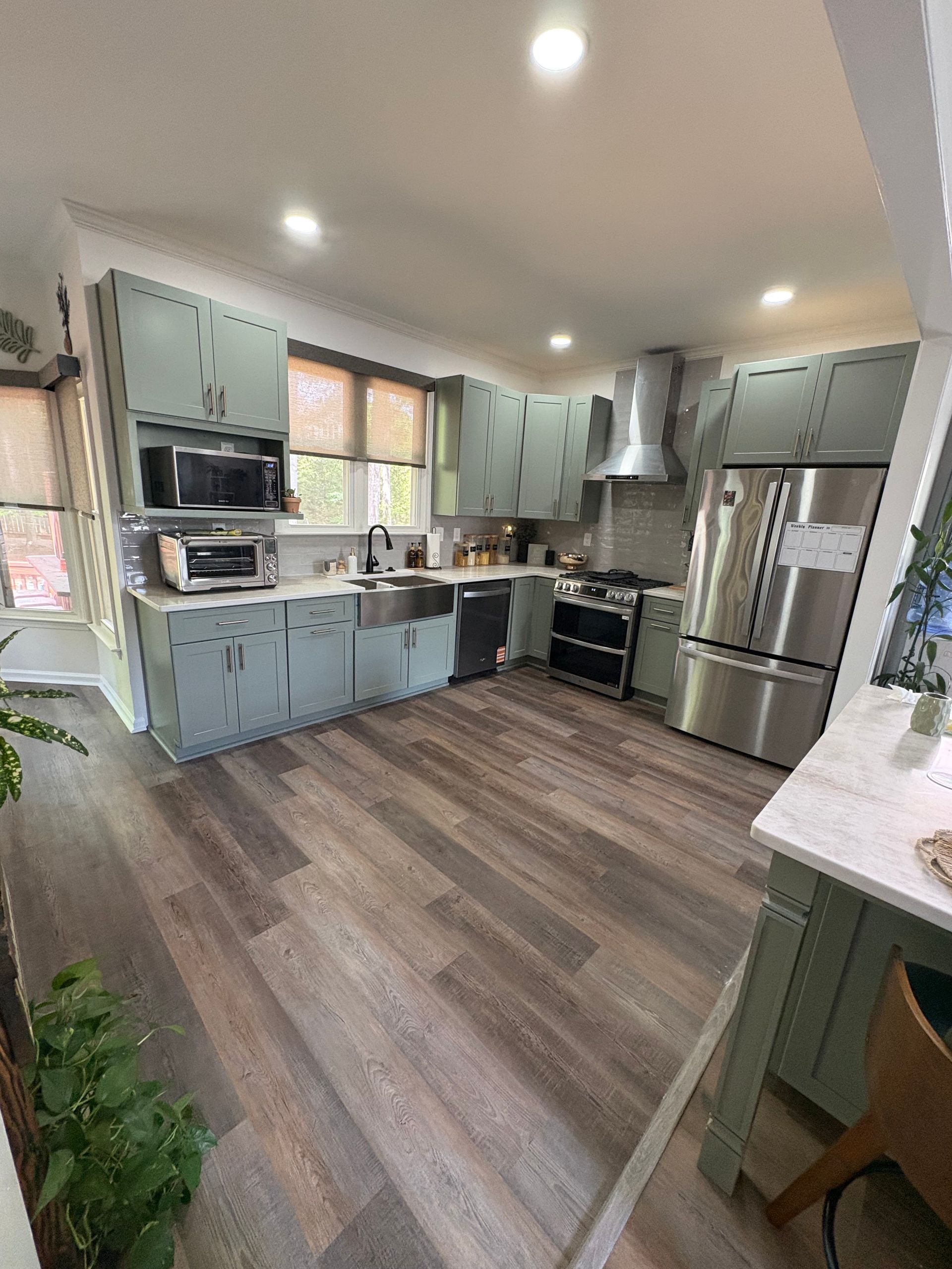 Bright kitchen with mint cabinets, stainless appliances, wood floors, and recessed lighting
