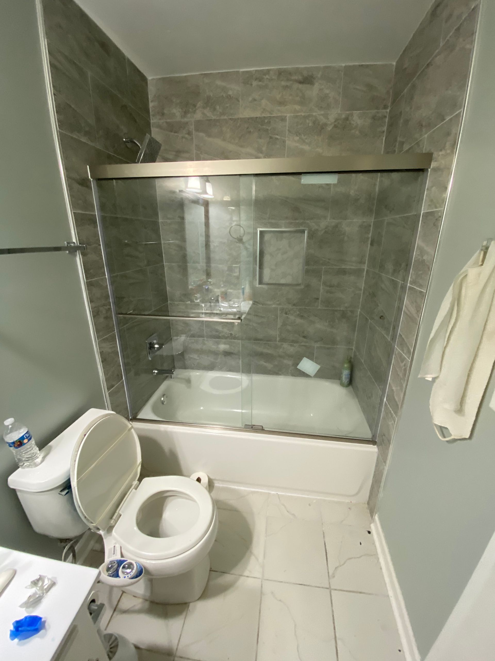 Small bathroom with toilet, vanity, and a glass-enclosed tub-shower with gray tile walls.