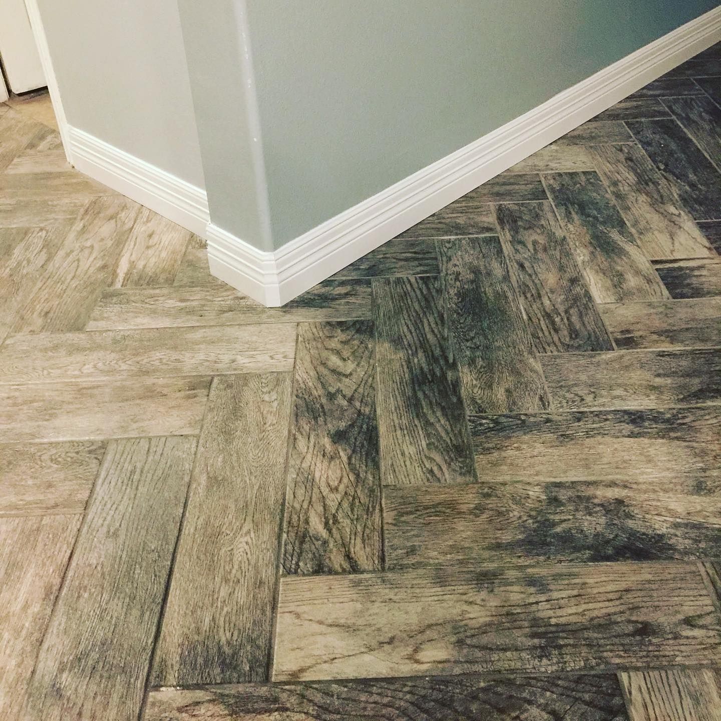 Corner of a room with gray walls and white baseboards over patterned wood-look flooring.