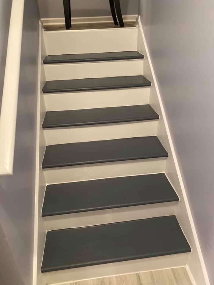 Narrow indoor staircase with dark gray steps, white sides, and a black handrail at the top