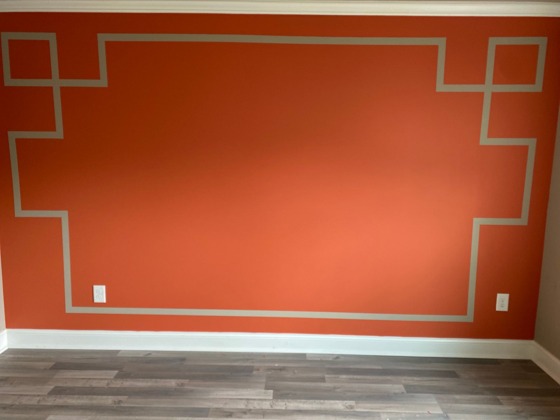 Orange accent wall with gray geometric trim above wood flooring and white baseboards