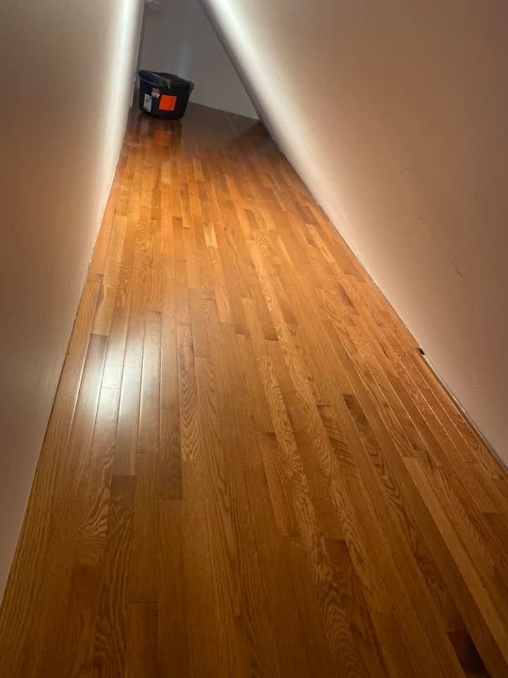 Narrow hallway with glossy hardwood floor and beige walls, with a black and orange bag at the far end