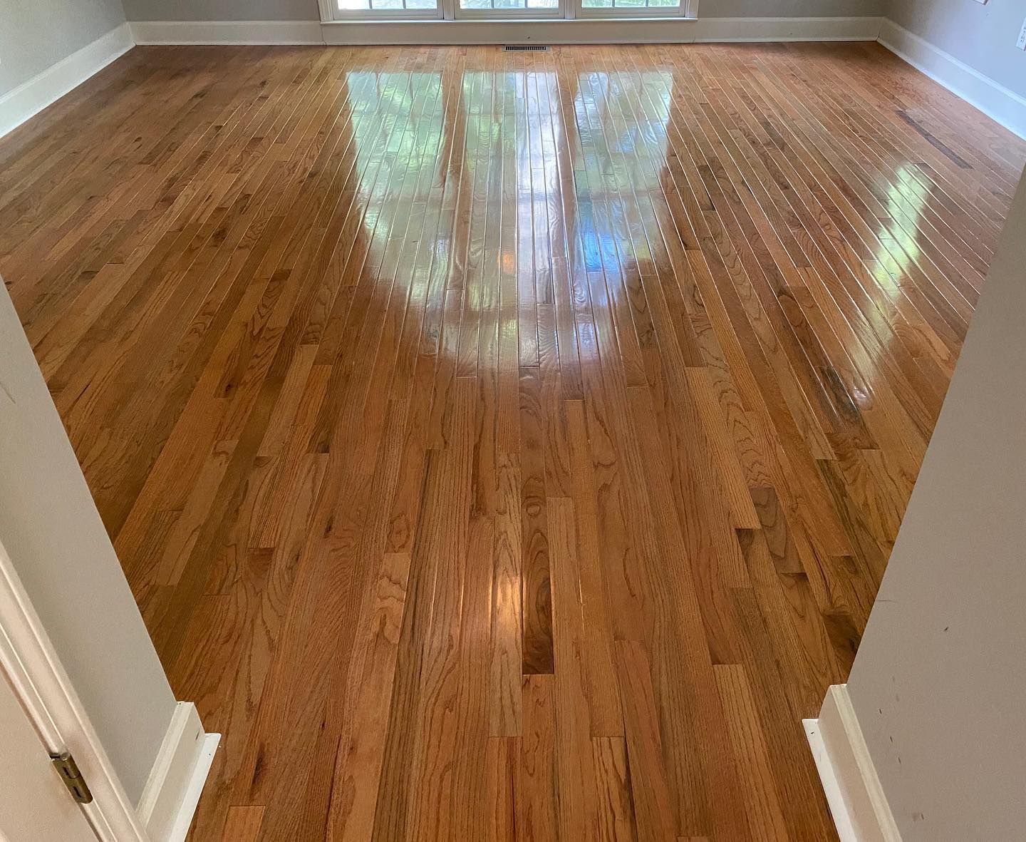 Empty room with polished hardwood floors and sunlight reflecting from a window